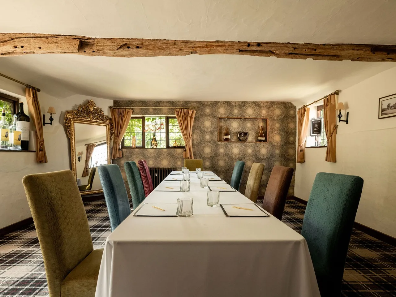 A cozy meeting or dining room with a long table, assorted colorful chairs, and rustic decor.