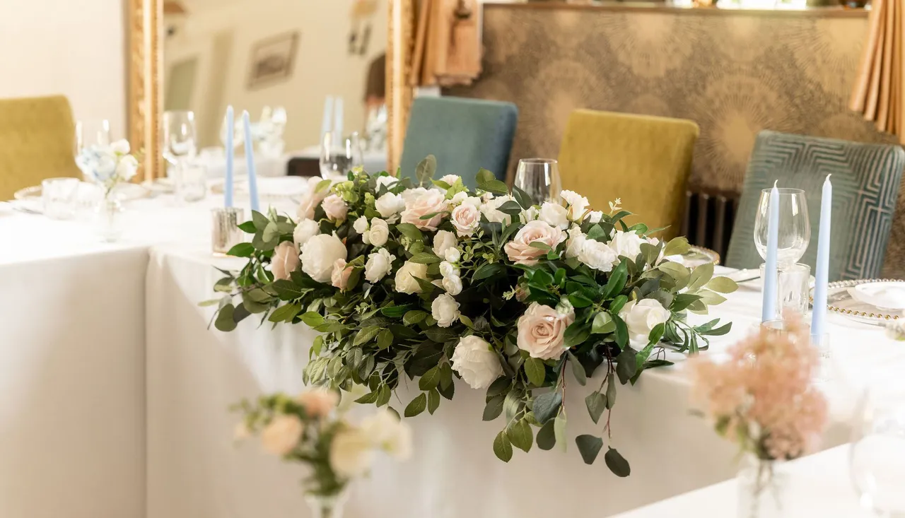 Elegant wedding table arrangement with white and blush pink flowers, greenery, and light blue candles.