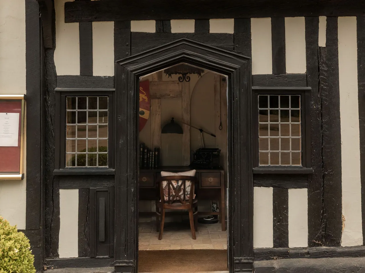 Entrance to a historic timber-framed building with a wooden desk and chair visible inside.