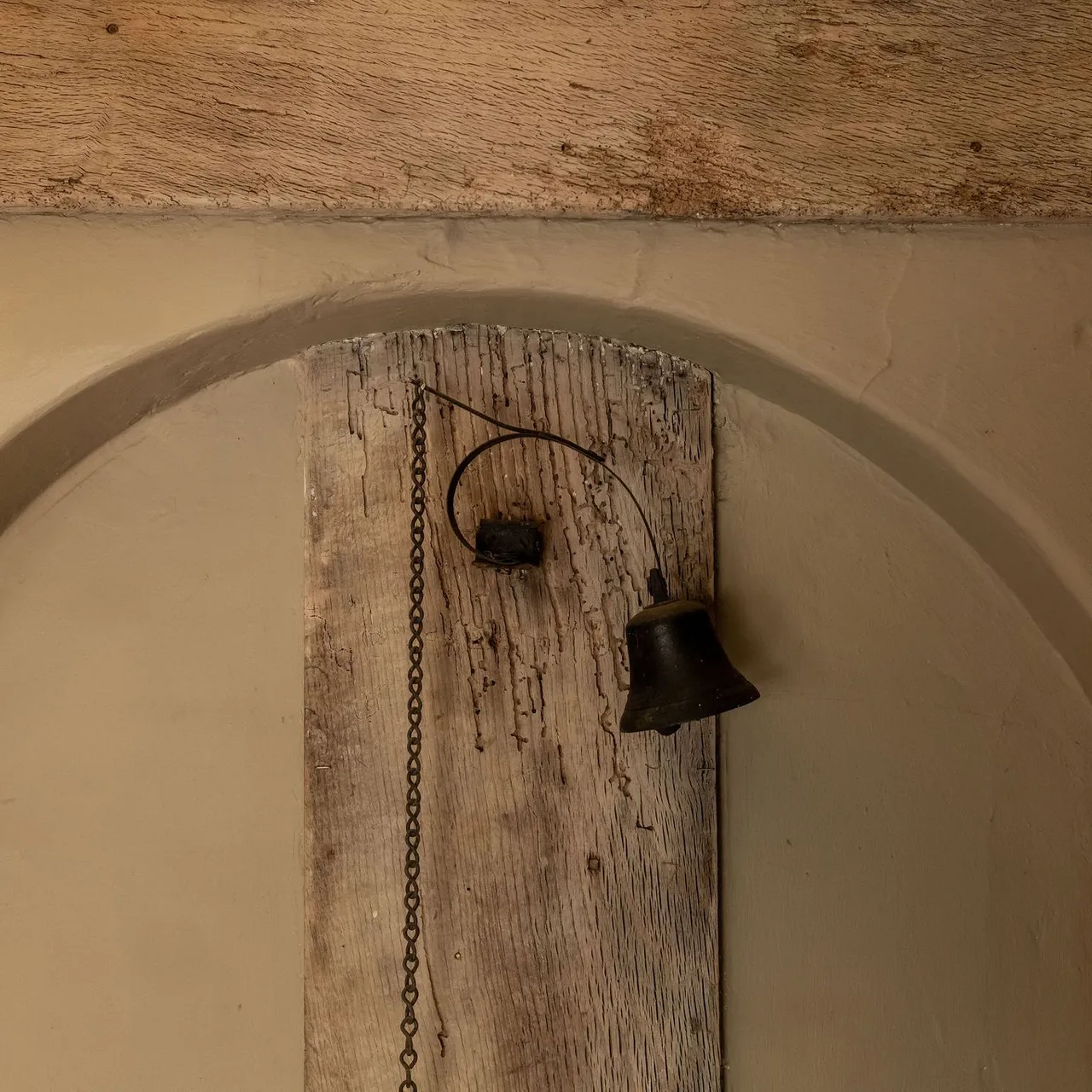 Old rustic metal bell attached to a wooden board with a hanging chain.