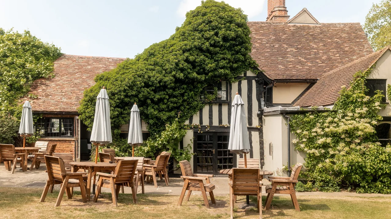 Outdoor patio with wooden tables and chairs in front of a charming, ivy-covered building