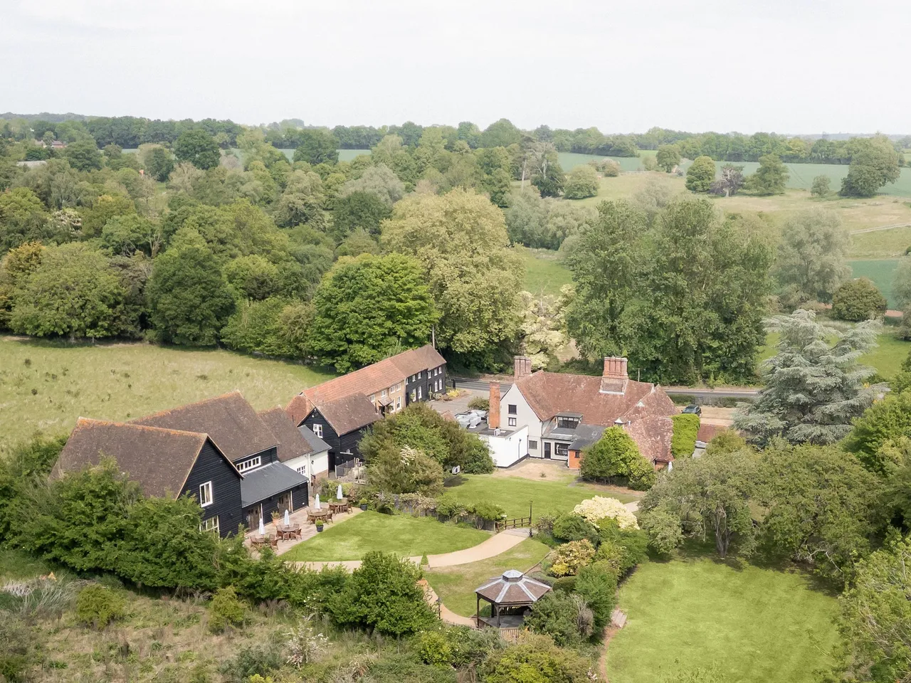 Aerial view of a countryside estate with several buildings, trees, gardens, and open green spaces.