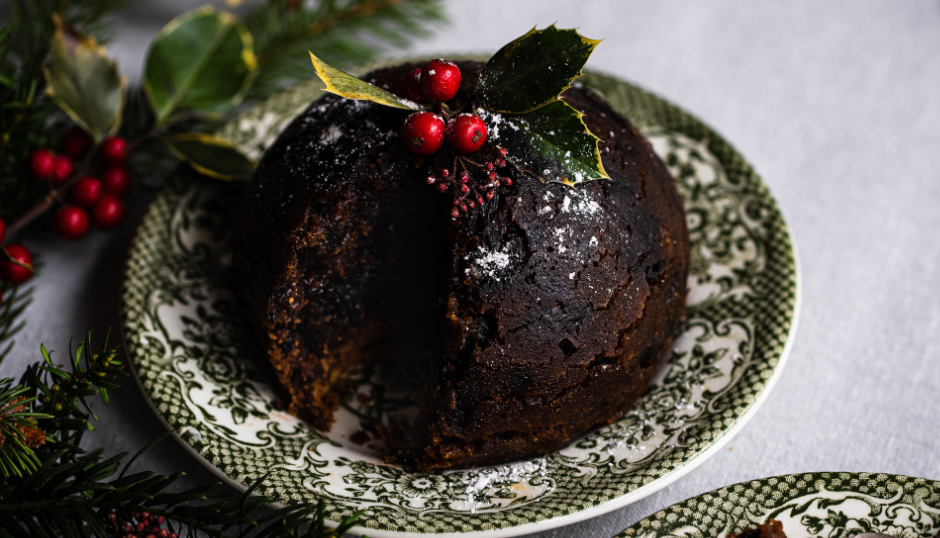 Traditional Christmas pudding decorated with holly and red berries on a patterned plate