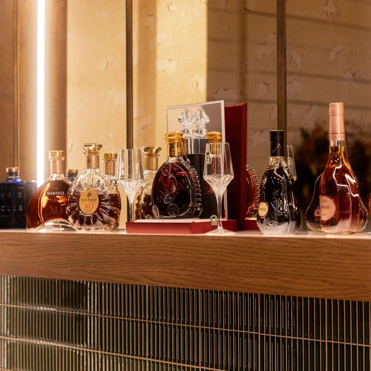 A collection of premium cognac and liquor bottles displayed on a wooden shelf with glassware.