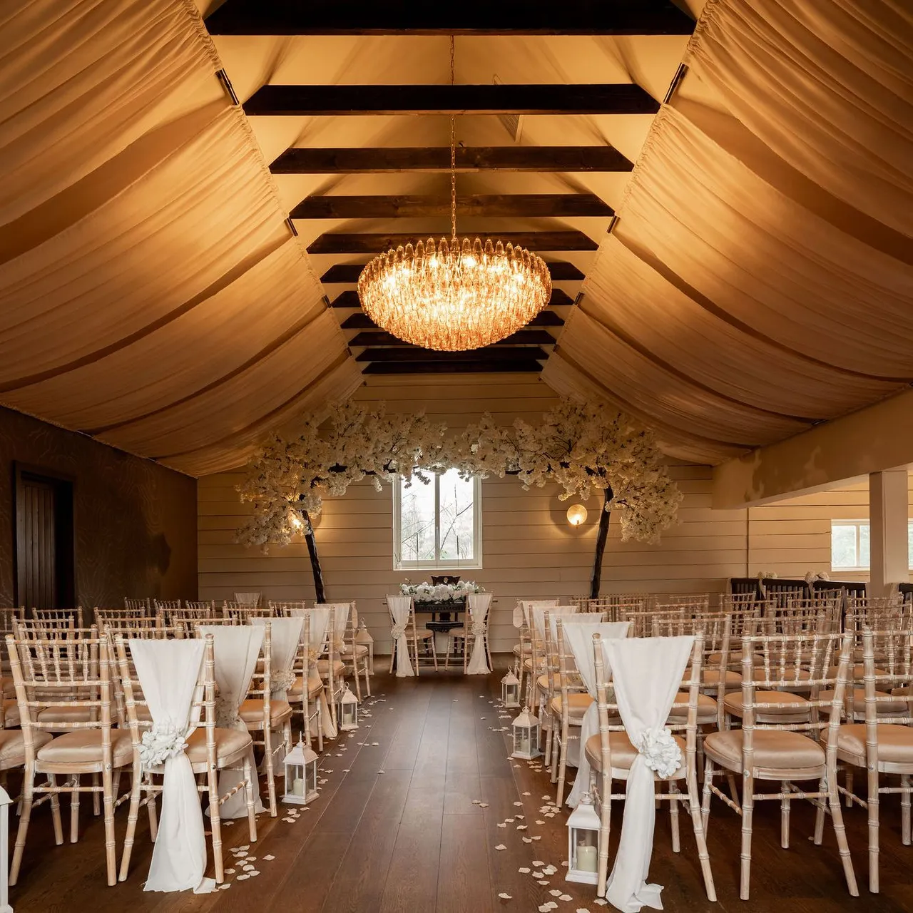 Elegant indoor wedding ceremony setup with rows of chairs, draped fabric ceiling, and a chandelier.