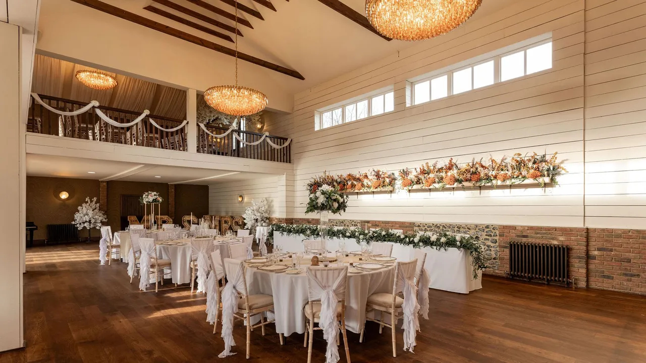 The Essex Barn dressed for a wedding, with round tables, white chair covers, floral garlands and chandeliers