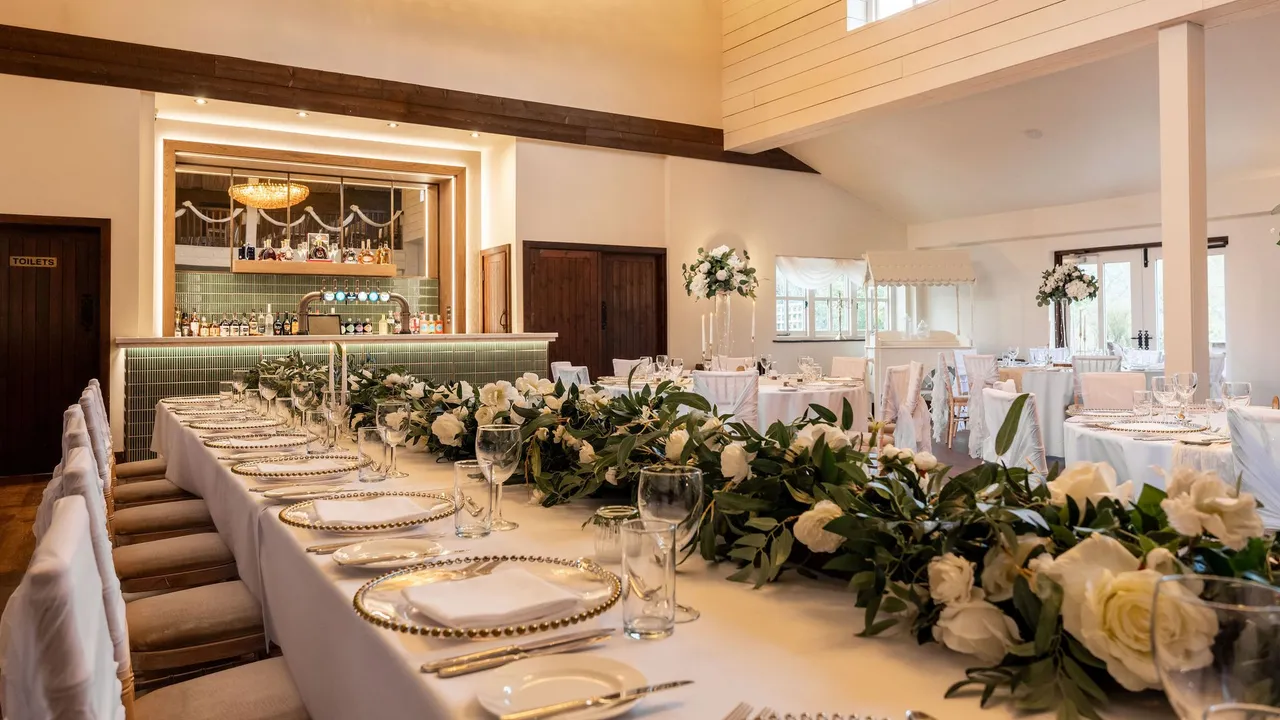 Elegantly decorated wedding reception hall with a long table adorned with white flowers and greenery, set for a formal meal.
