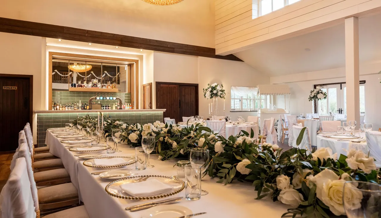 Elegantly decorated wedding reception hall with a long table adorned with white flowers and greenery, set for a formal meal.