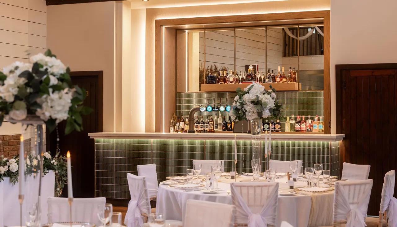 Elegant bar area with green tiles, mirrored backdrop, and wedding reception tables in front with white floral centerpieces.