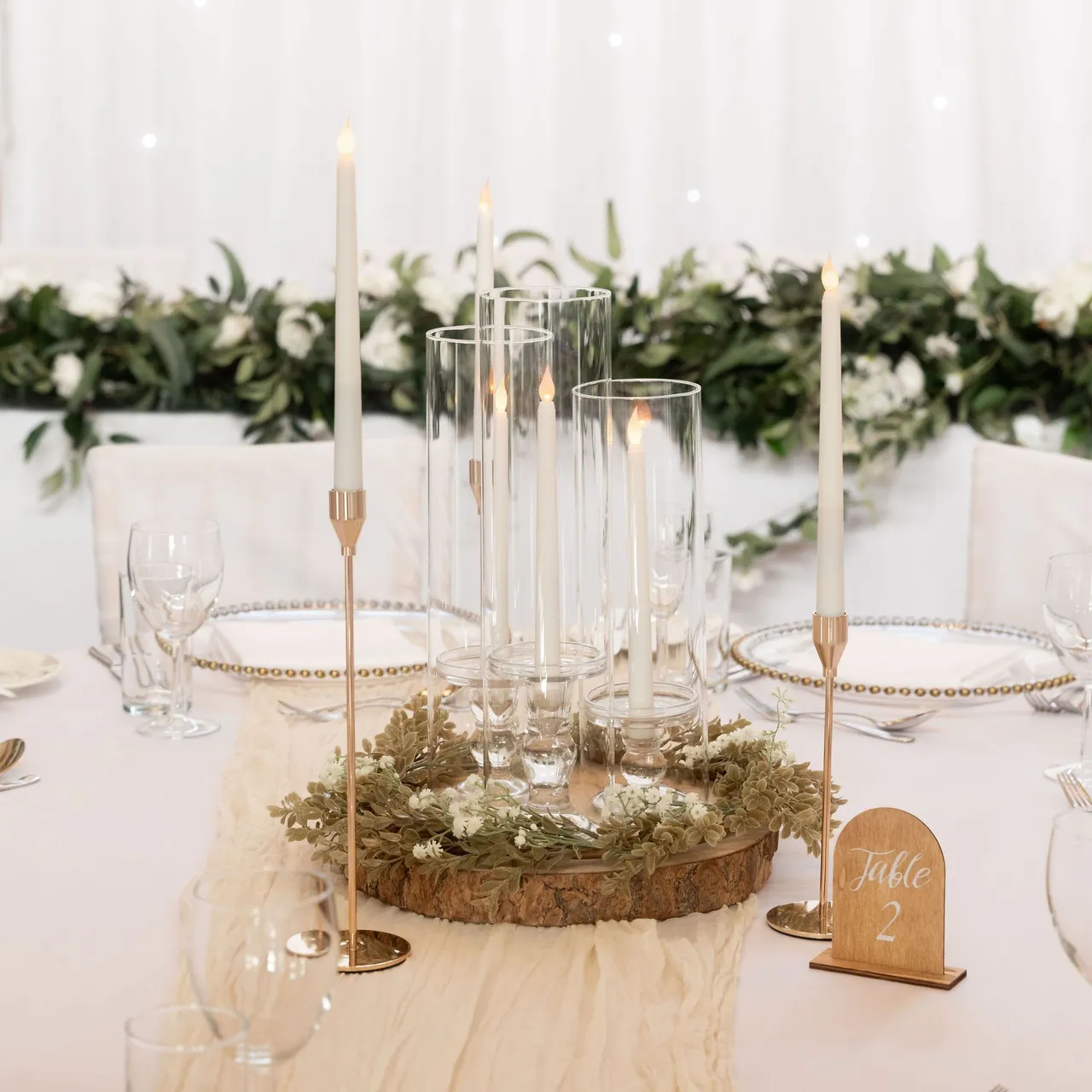 Elegant wedding table centerpiece with candles, greenery, and a Table 2 sign