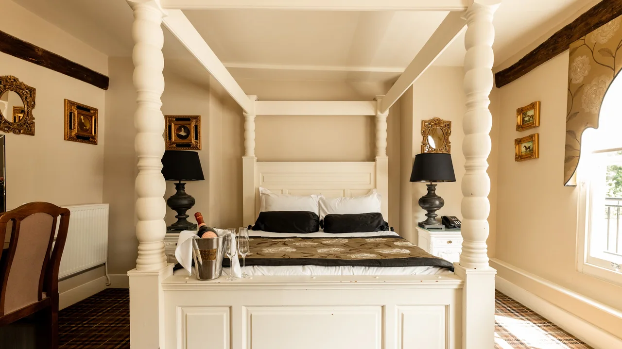 Elegant bedroom with a four-poster bed, bedside lamps, and champagne on the bed.