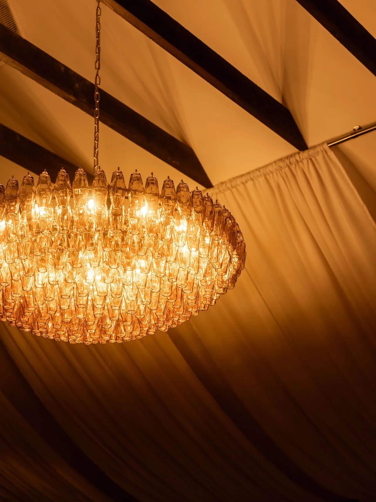 Ornate glass chandelier glowing warmly against the barn's timber ceiling